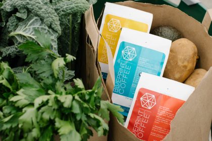 Bags of Red, Yellow, and Blue coffee blends in a paper grocery bag with lettuce and potatoes.