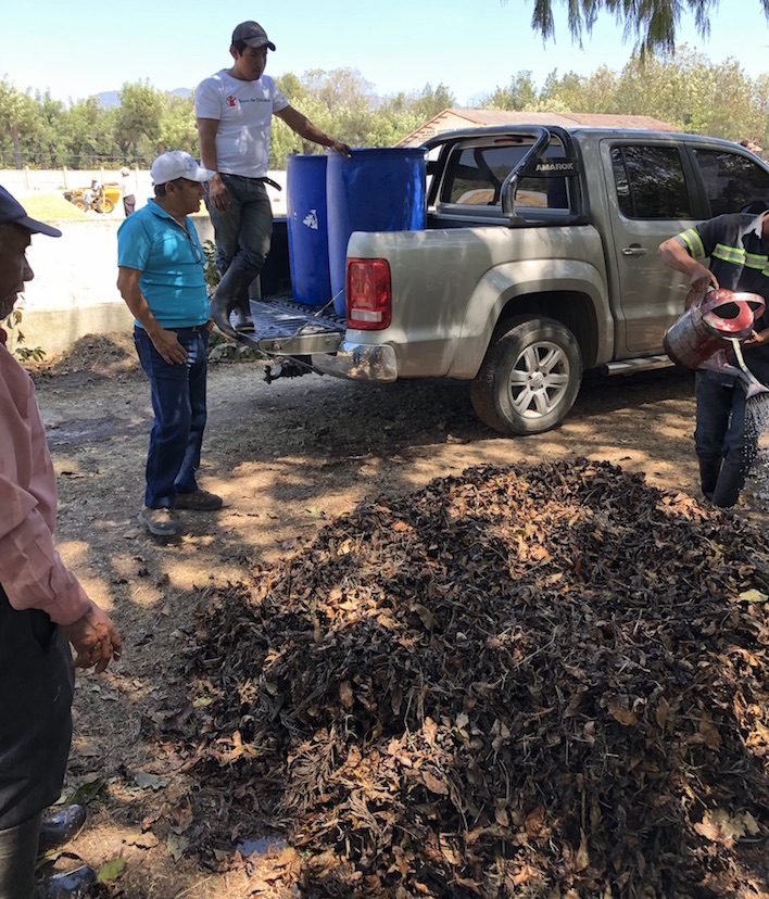 Coffee farmers look at their composting pile while standing next to a truck.