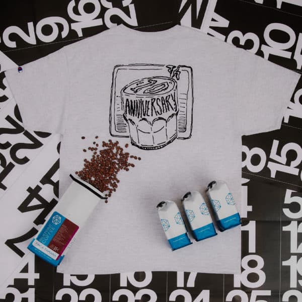 A Blueprint Coffee anniversary t-shirt on top of calendar pages with coffee beans spilled onto the shirt.