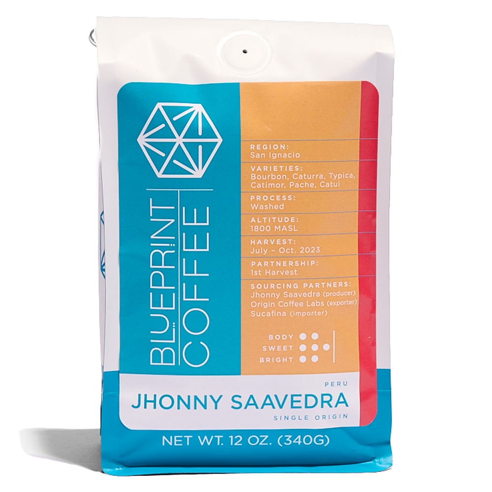 A 12-ounce bag of coffee beans with the Blueprint Coffee logo on the left side and the name Johnny Saavedra on the bottom. The bag is blue, yellow, red, and white.