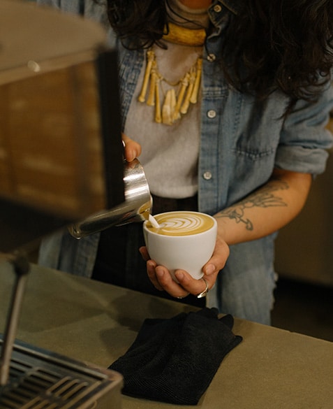 Ashley pours a cappuccino into a mug