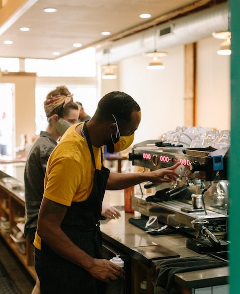 El Profile 9 El wears an orange mask and shirt, making an espresso behind the bar at Blueprint Coffee Delmar