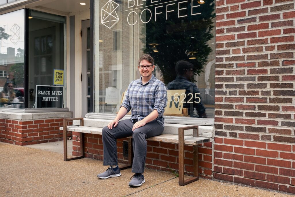 T sits on the wooden bench in front of our Delmar café and smiles at the camera