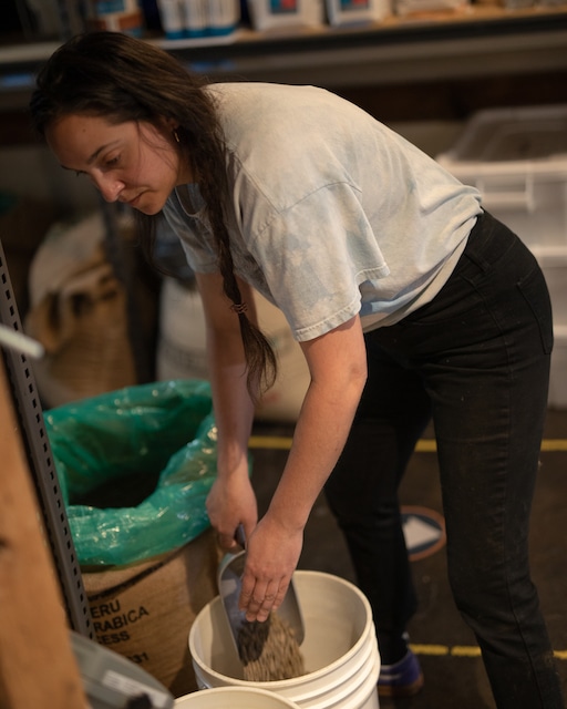 Marija scoops green coffee seeds into a white bucket
