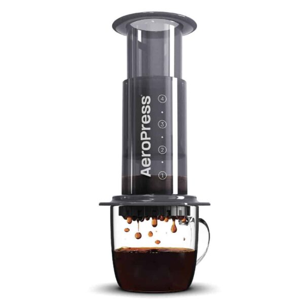 The aeropress coffee brewer sits atop a mug of coffee, which is translucent and shows brewed coffee dripping from the brewer into the cup.