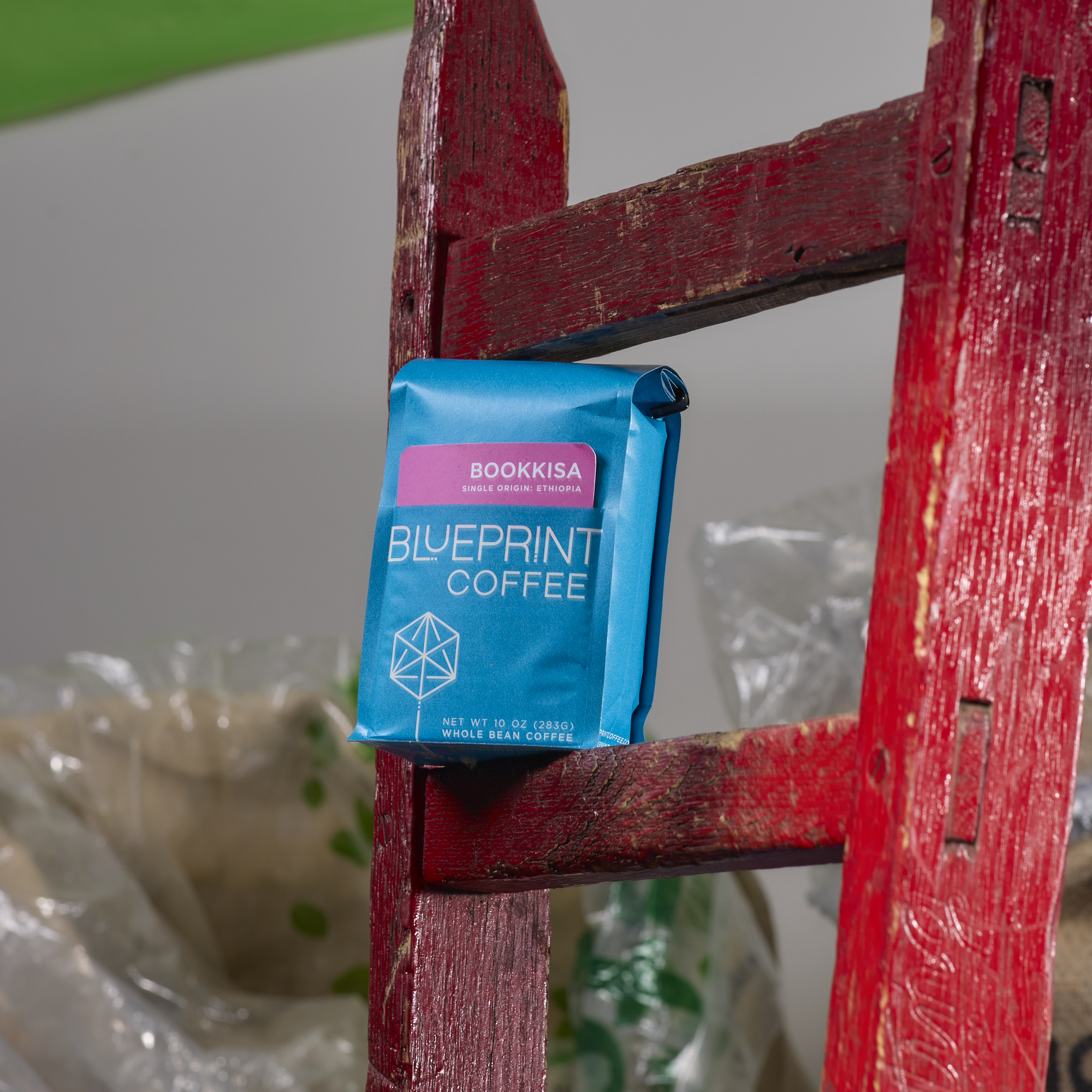 A bright blue 10 oz bag of Bookkisa, Ethiopia sits on a rung of a red wooden ladder in a warehouse