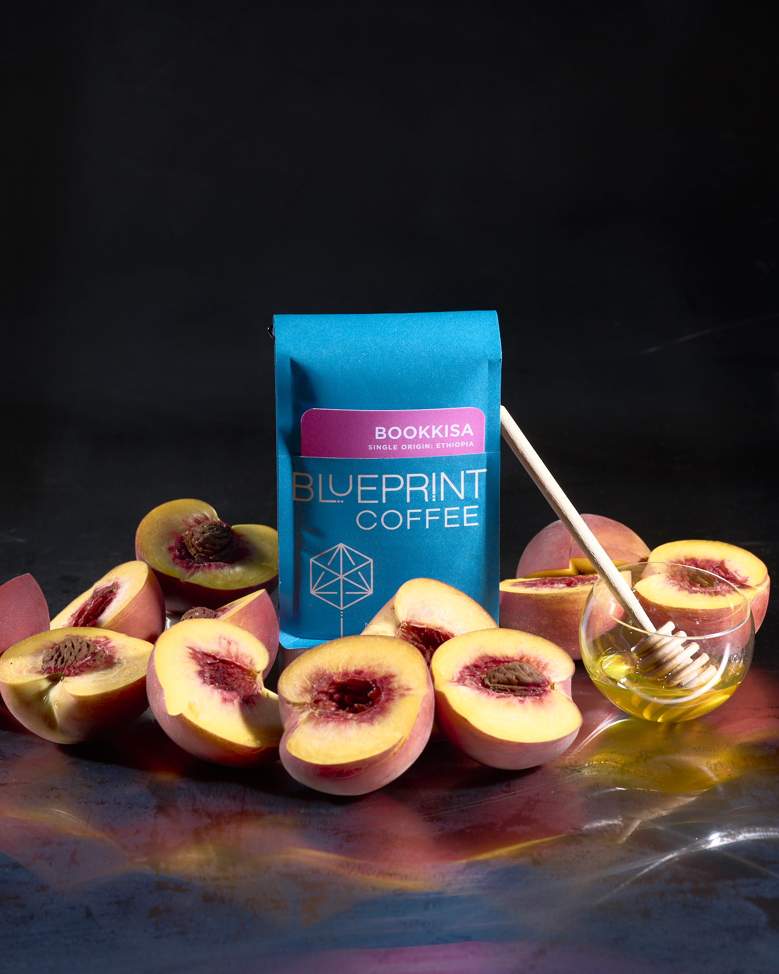 A blue 10-ounce bag of Bookkisa, Ethiopia surrounded by halved peaches and a bowl of honey