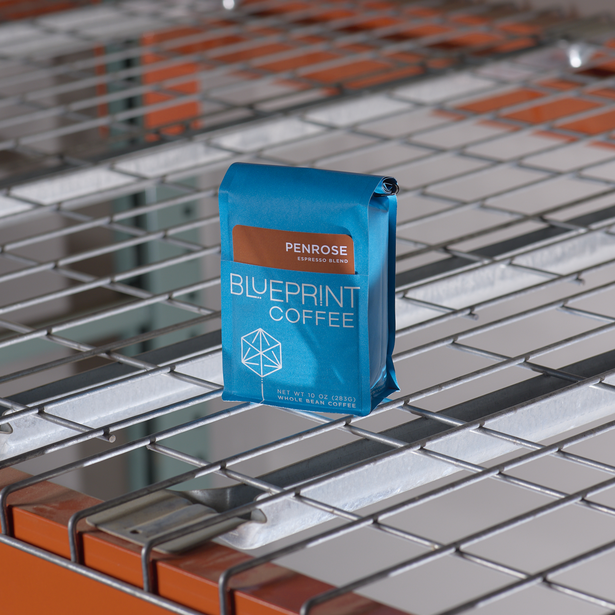 A blue 10-ounce bag of Penrose Espresso Blend on a metal wire warehouse shelf