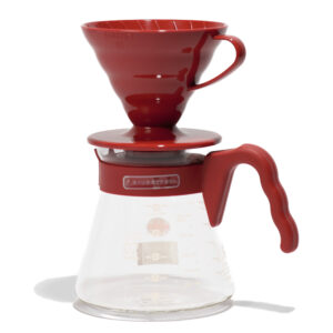 A red, plastic V60 coffee dripper sitting atop the included glass carafe with red handle.