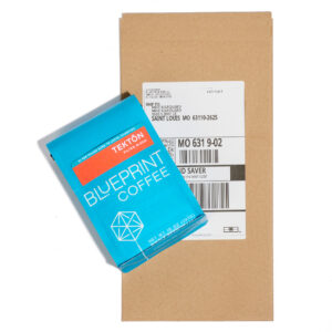A bag of Tektōn coffee beans on top of a craft paper mailing envelope.