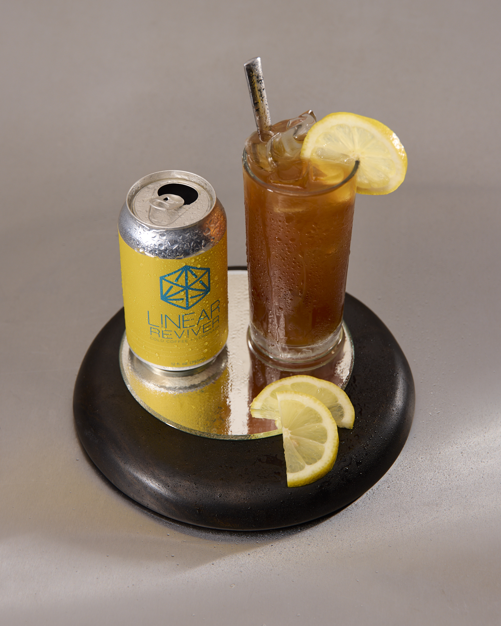 A glass of Linear Reviver arranged on a tray beside its empty yellow can and slices of lemon