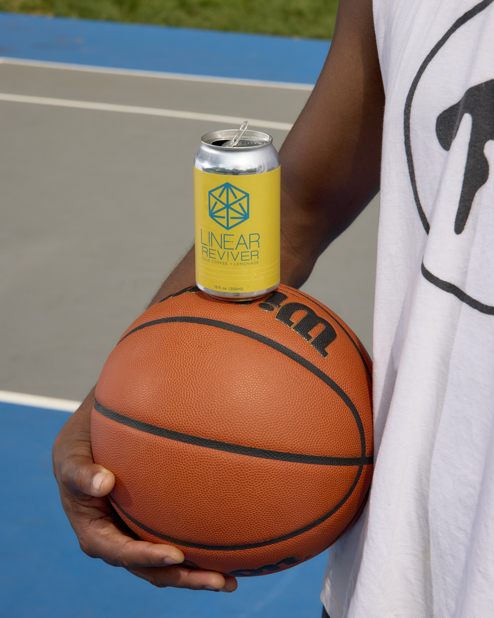 A man holds a basketball at his side with a yellow can of Linear Reviver balanced on top