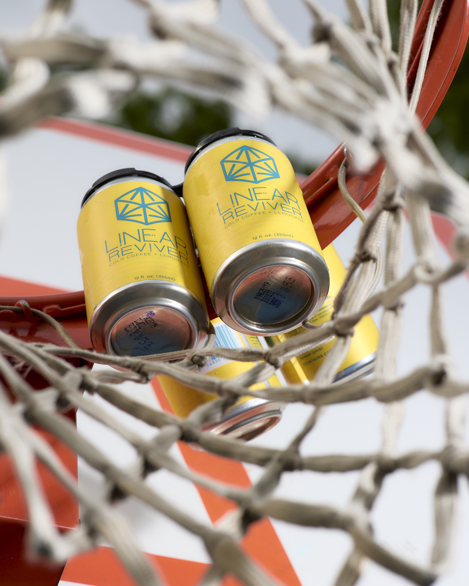 A 4-pack of Linear Reviver cans is placed atop the orange rim of a basketball net and views from below