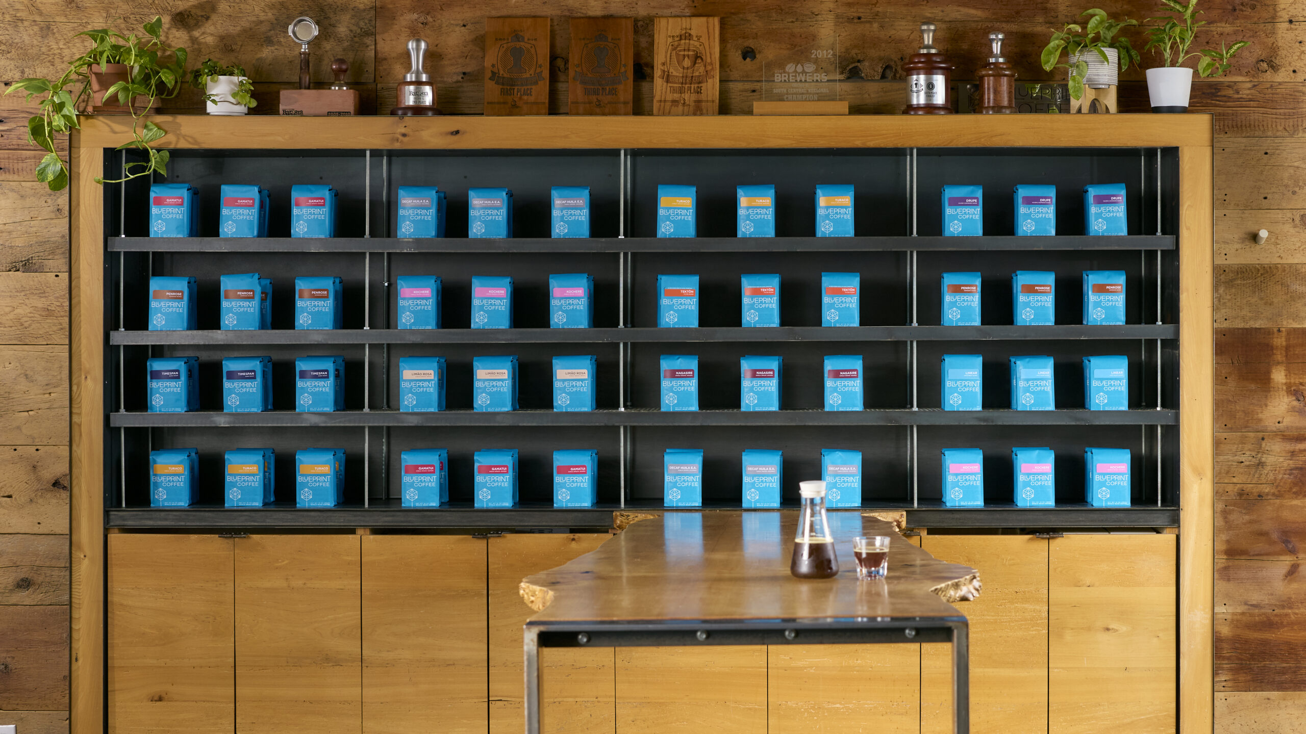 A retail shelf at Blueprint Coffee's Delmar Blvd. cafe is full of bright blue bags of coffee beans, labelled by cards of various bright colors.