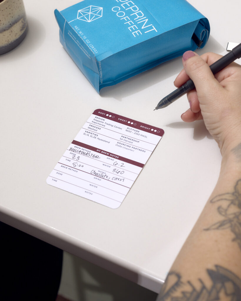 A person writes coffee notes on the interactive card included in their bag of Blueprint Coffee beans