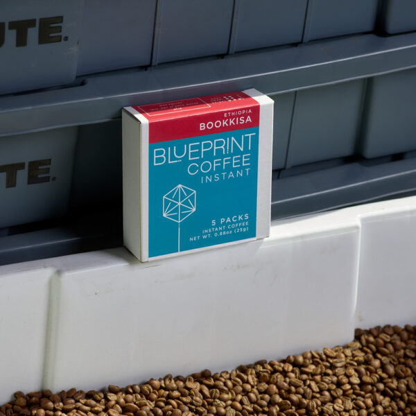 A box of Bookkisa, Ethiopia instant coffee rests on a tub of freshly roasted coffee beans.