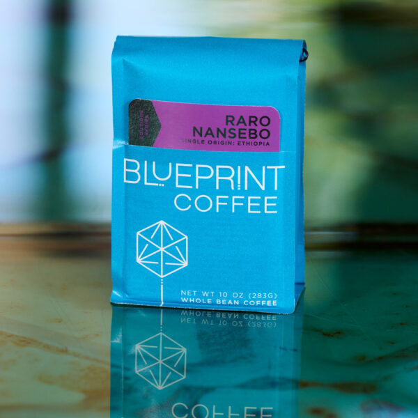 A 10-ounce bag of Raro Nansebo, Ethiopia coffee beans sits on a glass tabletop and reflects itself onto the surface.