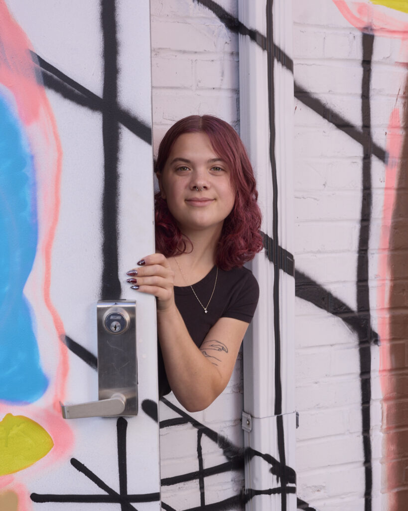 Sylvia peers from around the corner of a brightly painted wall