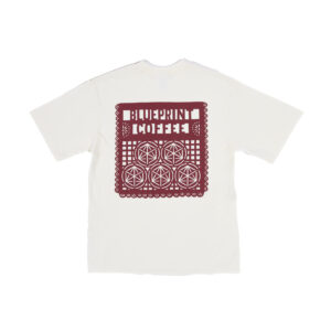 An off-white, boxy t-shirt printed with a dark red design inspired by papel picado with the words "Blueprint Coffee" incorporated into the intricate design
