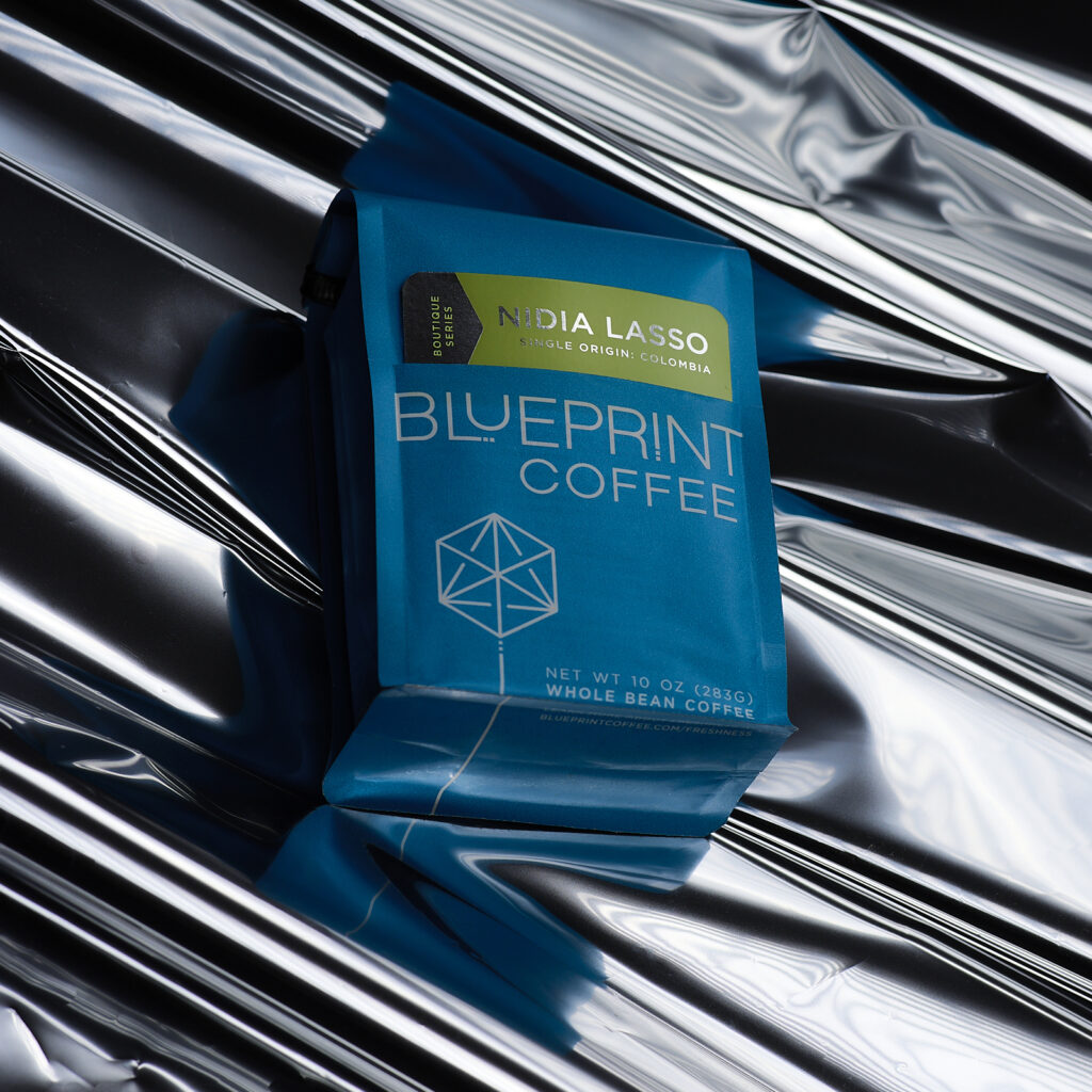 A blue bag of Nidia Lasso, Colombia roasted by Blueprint Coffee lies atop a crinkled sheet of silver metallic paper