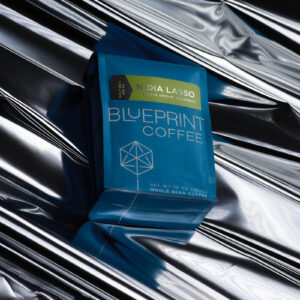 A blue bag of Nidia Lasso, Colombia roasted by Blueprint Coffee lies atop a crinkled sheet of silver metallic paper