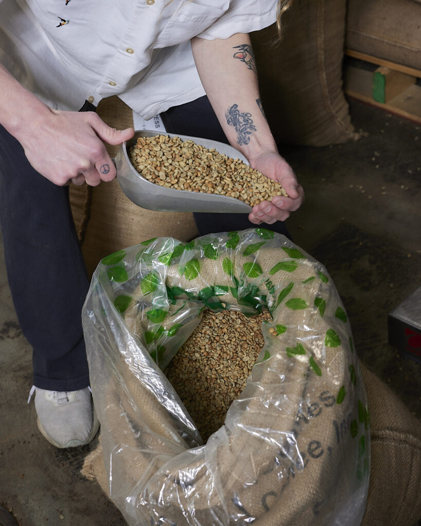 A person scooping green coffee from an open burlap bag at Blueprint Coffee's roastery 